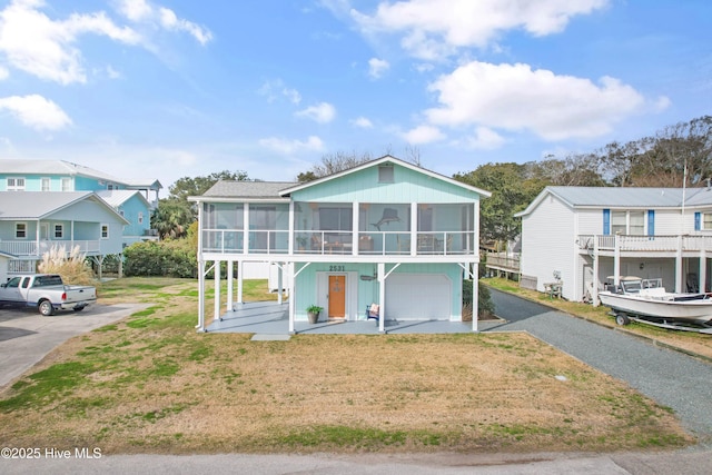 view of front of property featuring driveway, a sunroom, a residential view, an attached garage, and a front yard