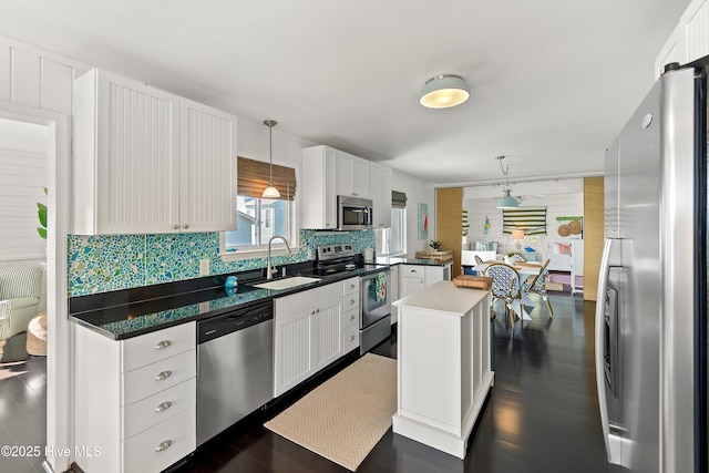 kitchen with appliances with stainless steel finishes, a center island, hanging light fixtures, white cabinetry, and a sink