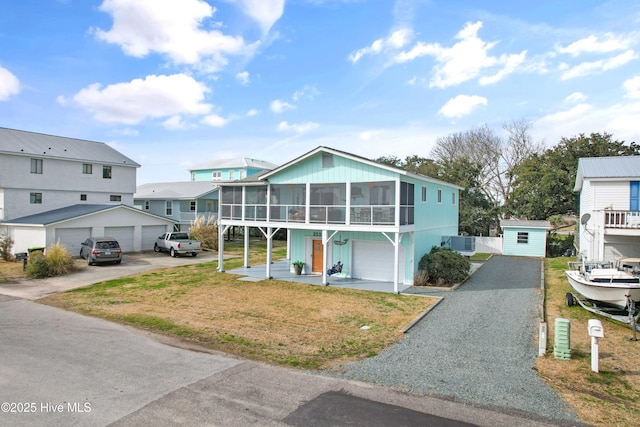 view of front of home featuring a garage, a sunroom, central air condition unit, and a front lawn