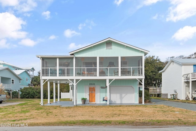 view of front of home featuring driveway, a sunroom, an attached garage, and a front yard