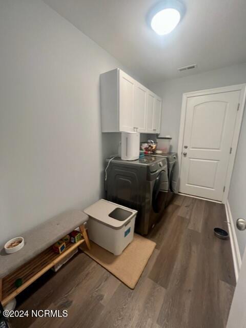 clothes washing area featuring dark wood-type flooring, cabinet space, visible vents, and washing machine and clothes dryer