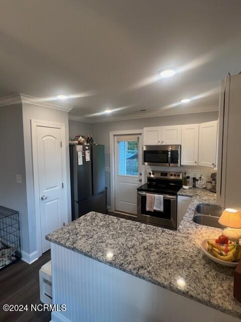 kitchen with dark wood-style flooring, light stone countertops, stainless steel appliances, crown molding, and white cabinetry