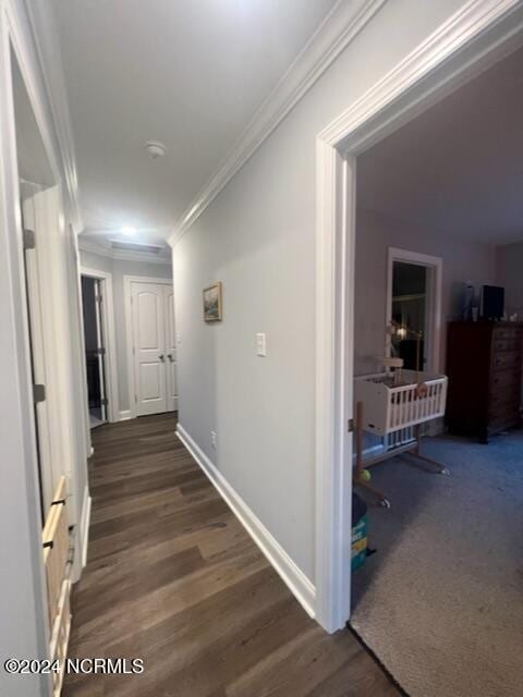 hallway with dark wood-type flooring, crown molding, and baseboards