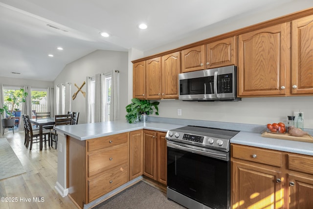 kitchen featuring light wood finished floors, lofted ceiling, appliances with stainless steel finishes, a peninsula, and light countertops