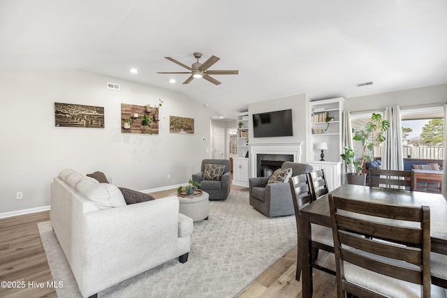 living area with vaulted ceiling, a fireplace, visible vents, and light wood-style floors