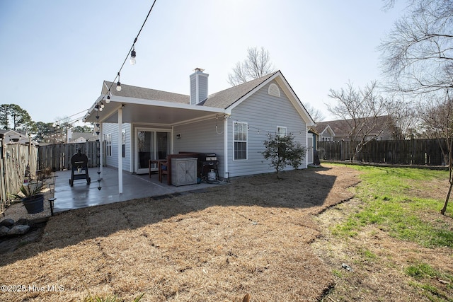 rear view of property with a yard, a chimney, a patio area, and a fenced backyard