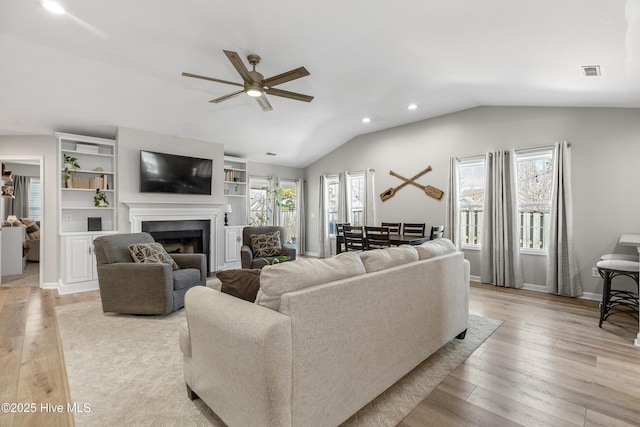 living room with light wood-type flooring, vaulted ceiling, visible vents, and a fireplace