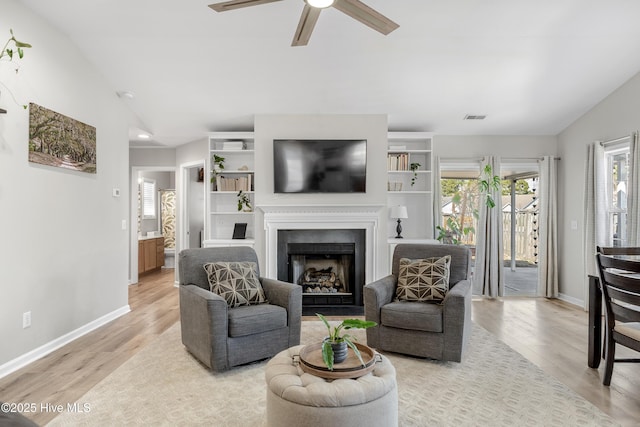 living room with a fireplace, lofted ceiling, visible vents, light wood-type flooring, and baseboards