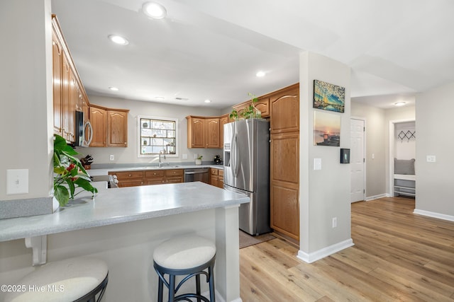 kitchen featuring recessed lighting, stainless steel appliances, a peninsula, light countertops, and light wood-type flooring