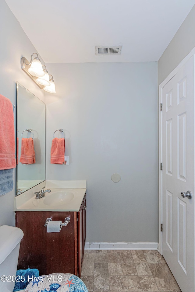 half bathroom with vanity, toilet, baseboards, and visible vents