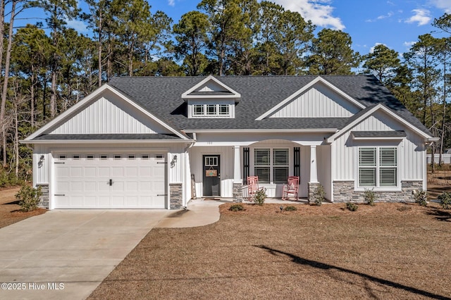 view of front of house featuring an attached garage, covered porch, a shingled roof, stone siding, and driveway