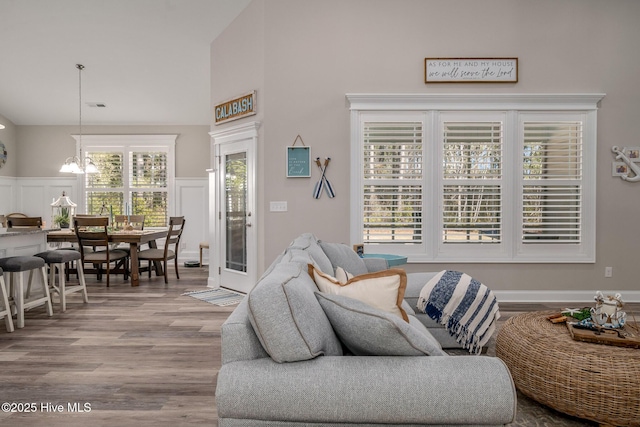 living area featuring a notable chandelier, visible vents, a decorative wall, wainscoting, and wood finished floors