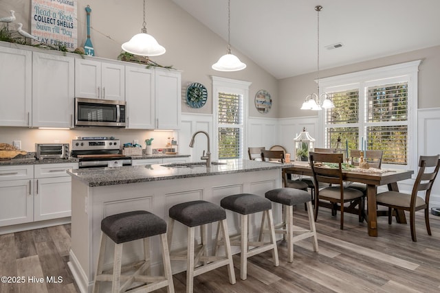 kitchen with a breakfast bar area, appliances with stainless steel finishes, white cabinetry, a sink, and an island with sink