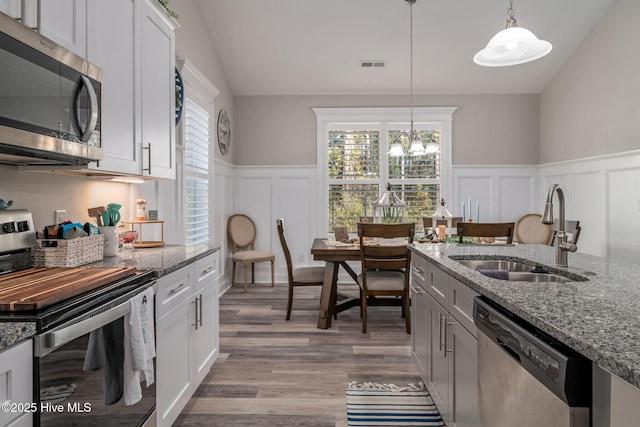 kitchen with stainless steel appliances, a sink, white cabinetry, dark stone counters, and decorative light fixtures