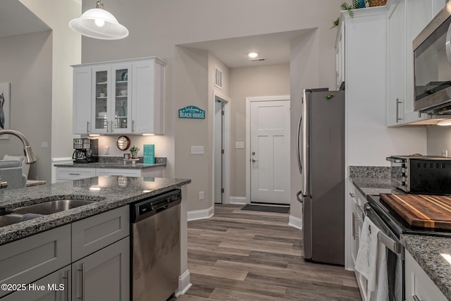 kitchen featuring stainless steel appliances, a sink, white cabinets, glass insert cabinets, and pendant lighting