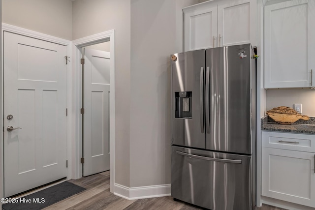 kitchen featuring baseboards, white cabinets, stainless steel refrigerator with ice dispenser, light wood finished floors, and dark stone countertops