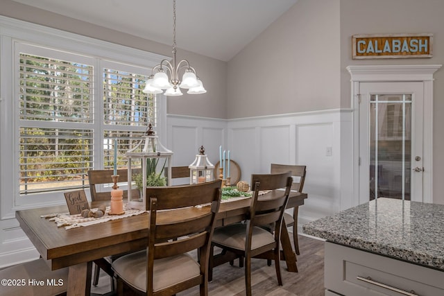 dining room with lofted ceiling, a decorative wall, an inviting chandelier, wainscoting, and wood finished floors