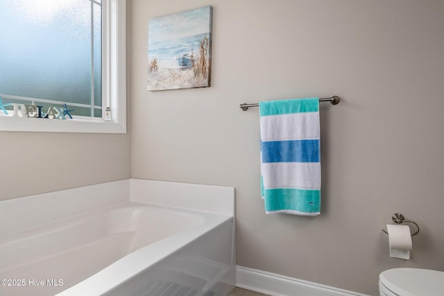 full bathroom featuring toilet, baseboards, and a bath