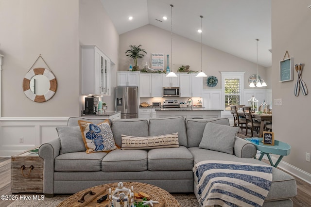 living room featuring a chandelier, a wainscoted wall, dark wood-type flooring, high vaulted ceiling, and a decorative wall