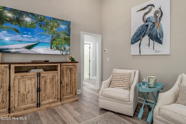 sitting room featuring light wood-style floors, a high ceiling, and baseboards