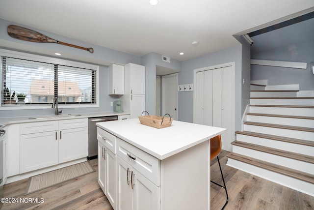 kitchen with light wood finished floors, white cabinets, a breakfast bar area, a sink, and stainless steel dishwasher