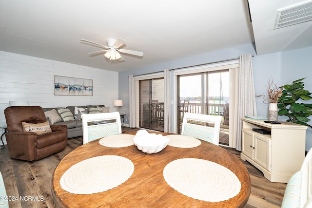 dining room featuring an accent wall, visible vents, ceiling fan, and wood finished floors