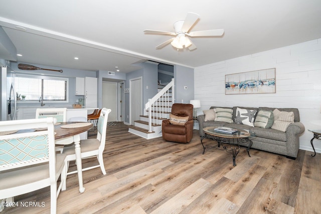 living room featuring light wood-type flooring, ceiling fan, stairs, and visible vents