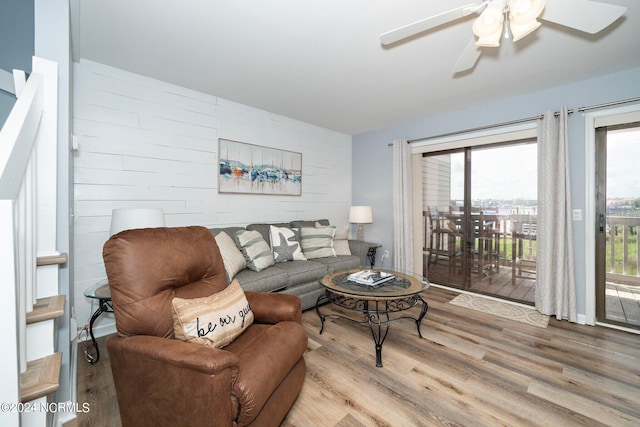 living area with ceiling fan, wood walls, and wood finished floors