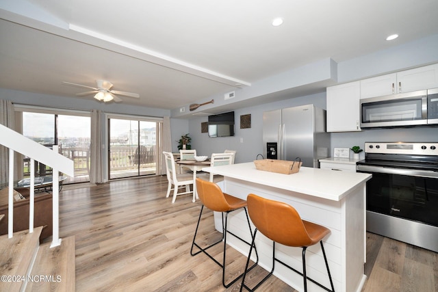 kitchen with stainless steel appliances, light countertops, light wood-style flooring, white cabinets, and a kitchen island