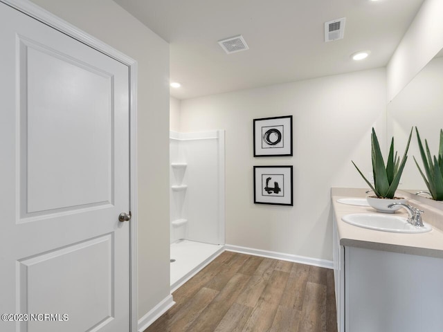 full bath with wood finished floors, visible vents, a sink, a walk in shower, and baseboards