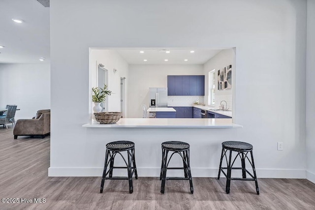 kitchen featuring a peninsula, a breakfast bar, a sink, light countertops, and light wood-type flooring