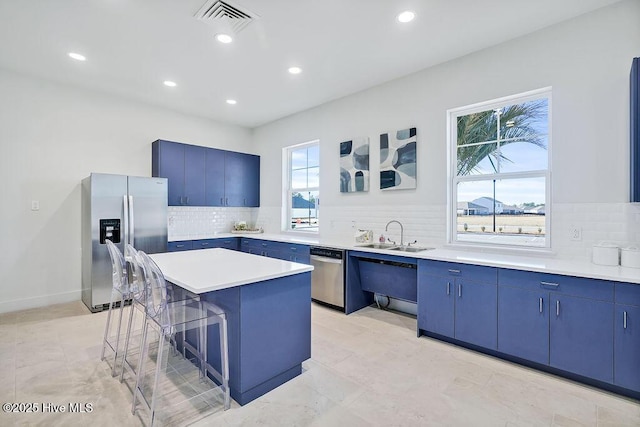 kitchen featuring a breakfast bar, light countertops, appliances with stainless steel finishes, a kitchen island, and a sink