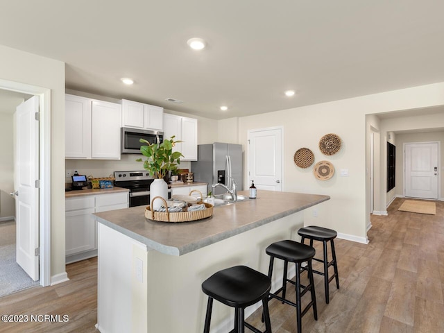 kitchen featuring a center island with sink, appliances with stainless steel finishes, a breakfast bar, light wood-type flooring, and white cabinetry