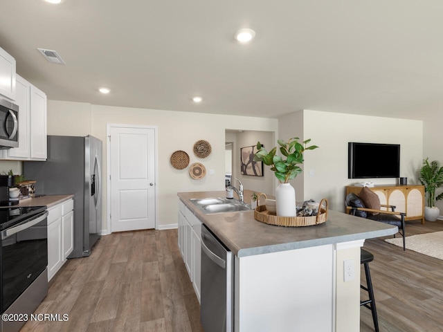 kitchen with a kitchen island with sink, stainless steel appliances, a sink, visible vents, and white cabinets