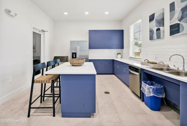 kitchen featuring appliances with stainless steel finishes, a breakfast bar area, a center island, light countertops, and blue cabinetry