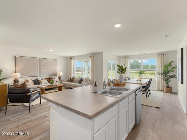 kitchen featuring stainless steel dishwasher, open floor plan, white cabinets, a sink, and an island with sink