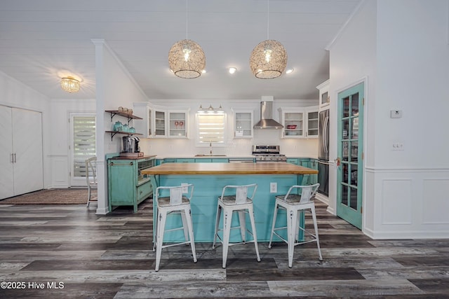 kitchen featuring white cabinets, wall chimney exhaust hood, butcher block countertops, glass insert cabinets, and appliances with stainless steel finishes