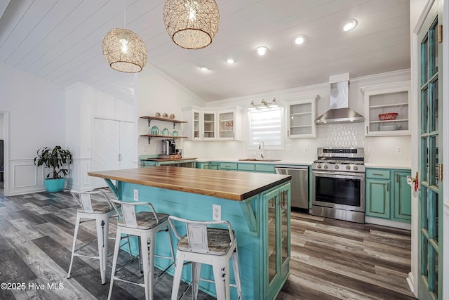 kitchen with open shelves, butcher block countertops, stainless steel appliances, wall chimney exhaust hood, and glass insert cabinets