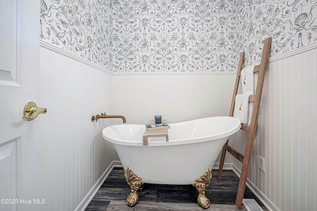 full bathroom with wood finished floors, baseboards, a freestanding bath, wainscoting, and wallpapered walls