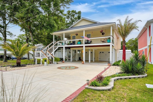 coastal home with covered porch, stairway, a carport, driveway, and a front lawn