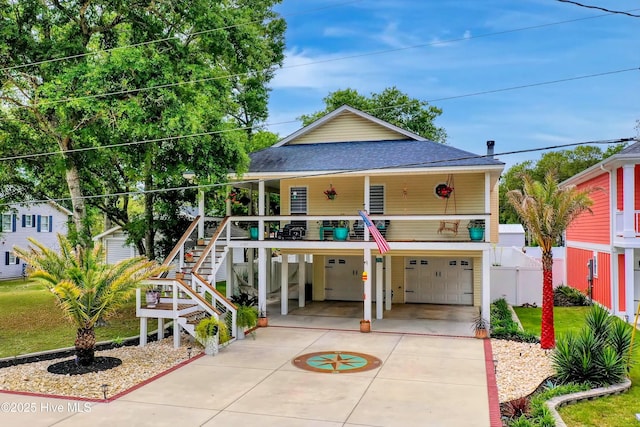 beach home with a shingled roof, concrete driveway, an attached garage, stairs, and a carport