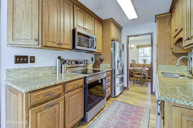 kitchen with a sink, light wood-style floors, light stone countertops, and stainless steel appliances