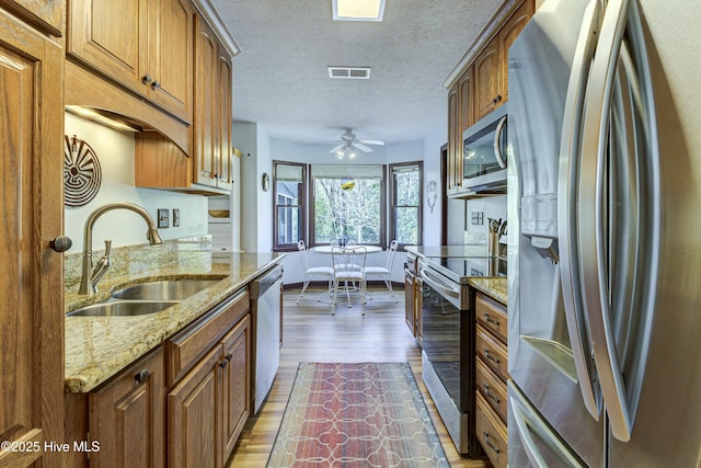 kitchen with visible vents, brown cabinets, wood finished floors, stainless steel appliances, and a sink