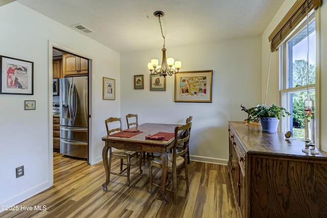 dining area with light wood-type flooring, baseboards, a textured ceiling, and visible vents