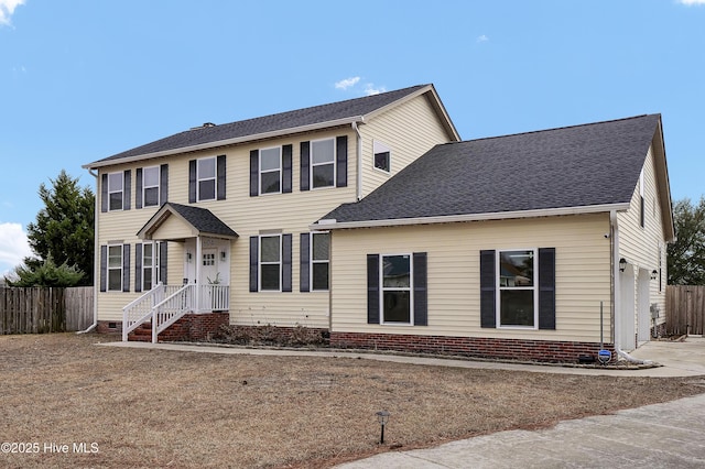 colonial-style house featuring fence, driveway, and roof with shingles