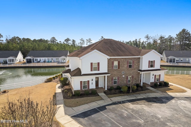 view of front of home with a residential view, a water view, fence, and brick siding