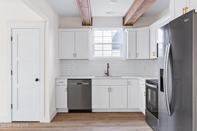 kitchen featuring appliances with stainless steel finishes, white cabinets, a sink, light wood-type flooring, and beamed ceiling