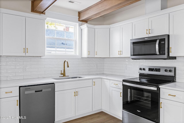 kitchen with a sink, light countertops, appliances with stainless steel finishes, backsplash, and beam ceiling