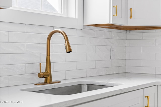 interior details with light stone countertops, a sink, white cabinetry, and decorative backsplash