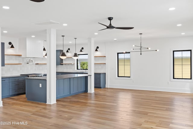 kitchen featuring light wood-style floors, backsplash, open shelves, dark countertops, and decorative light fixtures